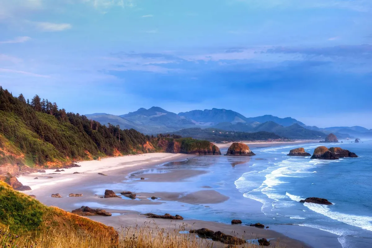 A captivating sunset over the Pacific, with golden light reflecting off the waves and rock formations in the distance. The sky is painted with warm hues, and the untouched beach invites leisurely evening walks or beach picnics.