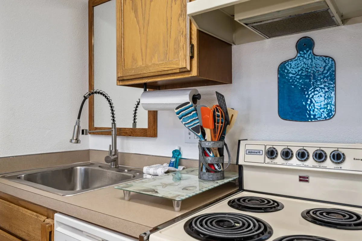 A cozy interior shot of a kitchen area, complete with a sink, stove, utensils, and meal prep essentials. The homey atmosphere highlights the family-friendly amenity of being able to prepare meals and gather comfortably within the condo.