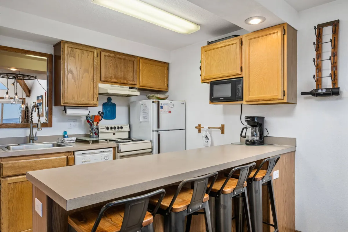 A close-up view of the kitchen's bar counter, flanked by wooden cabinets, stainless steel appliances, and a deep sink. The layout highlights the functional and social aspects of the kitchen, suggesting an ideal spot for breakfast or casual conversation.