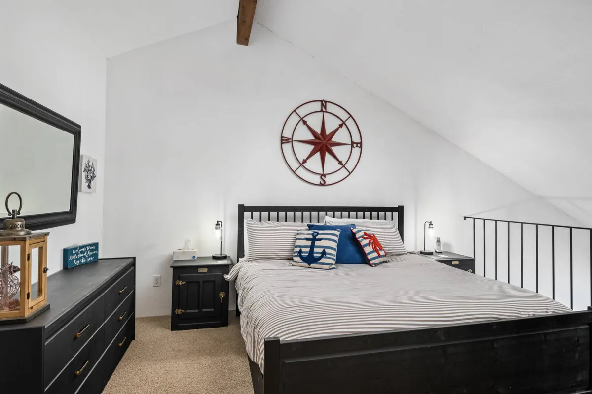 A sunlit bedroom with striped bedding, star compass wall décor, and decorative pillows. The space feels open and airy, with natural light streaming in, making it perfect for waking up to the sounds and sights of the ocean just beyond.