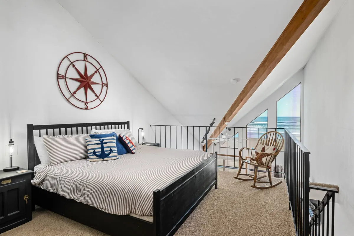 A serene bedroom with striped linens, nautical-themed pillows, a star compass wall decor, and a rocking chair by the window. The space is filled with soft natural light and offers a tranquil, cozy retreat.