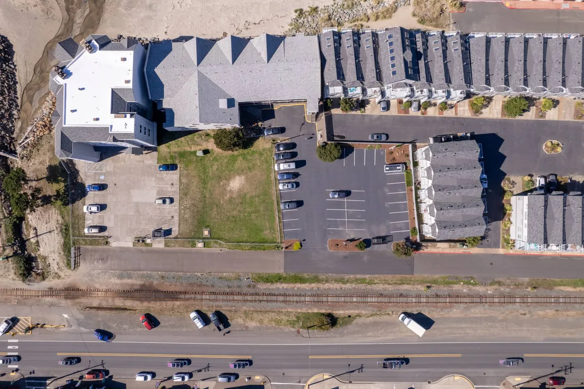 This image features the exterior of a large building structure that houses several neatly arranged townhouses, with a clear view of a spacious parking area in the foreground and the nearby beach visible in the distance. The overall atmosphere is casual and inviting, suggesting easy arrivals and community gathering spaces.