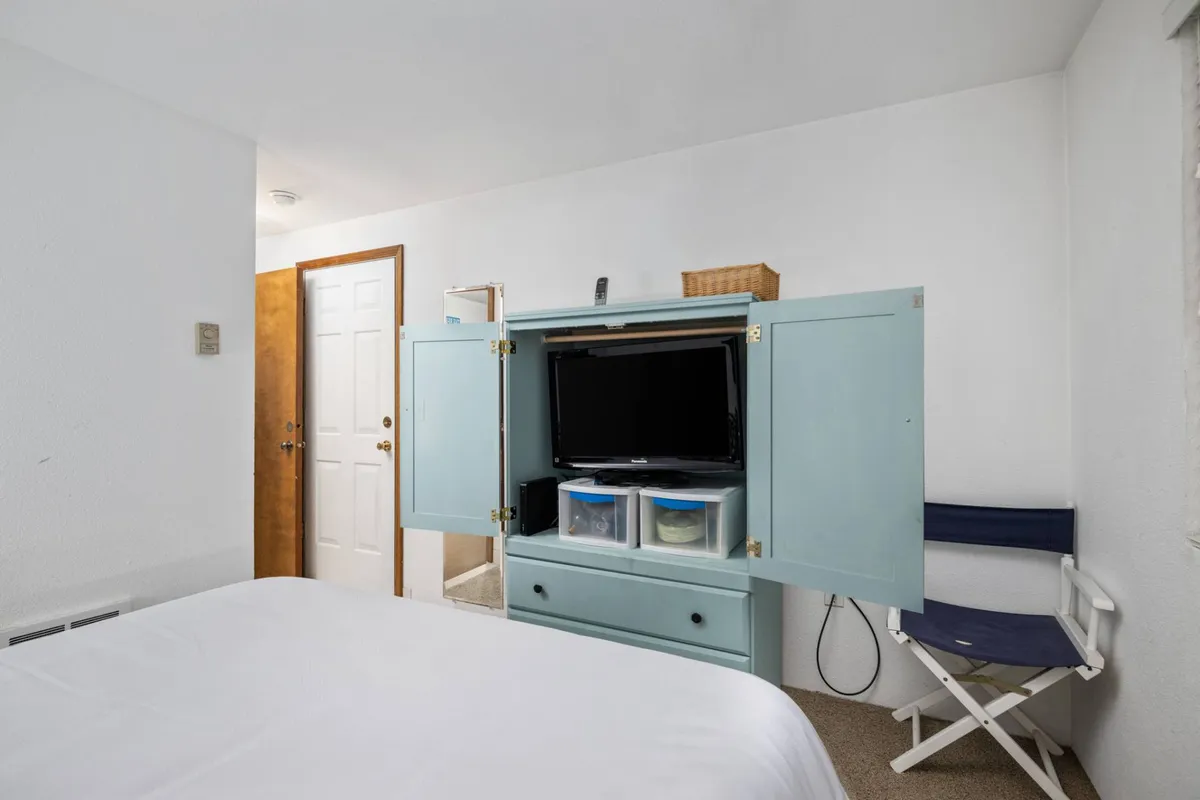 A cozy bed faces an open cabinet with a smart TV, set in a comfortable, well-lit room. The scene is welcoming and suggests both relaxation and the option for leisure time, such as enjoying a movie after a productive or inspiring day.